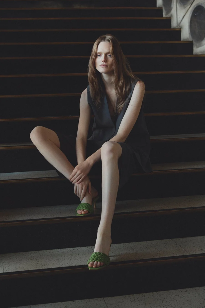 暗い階段に座り、緑のサンダルを履いた女性のポートレート