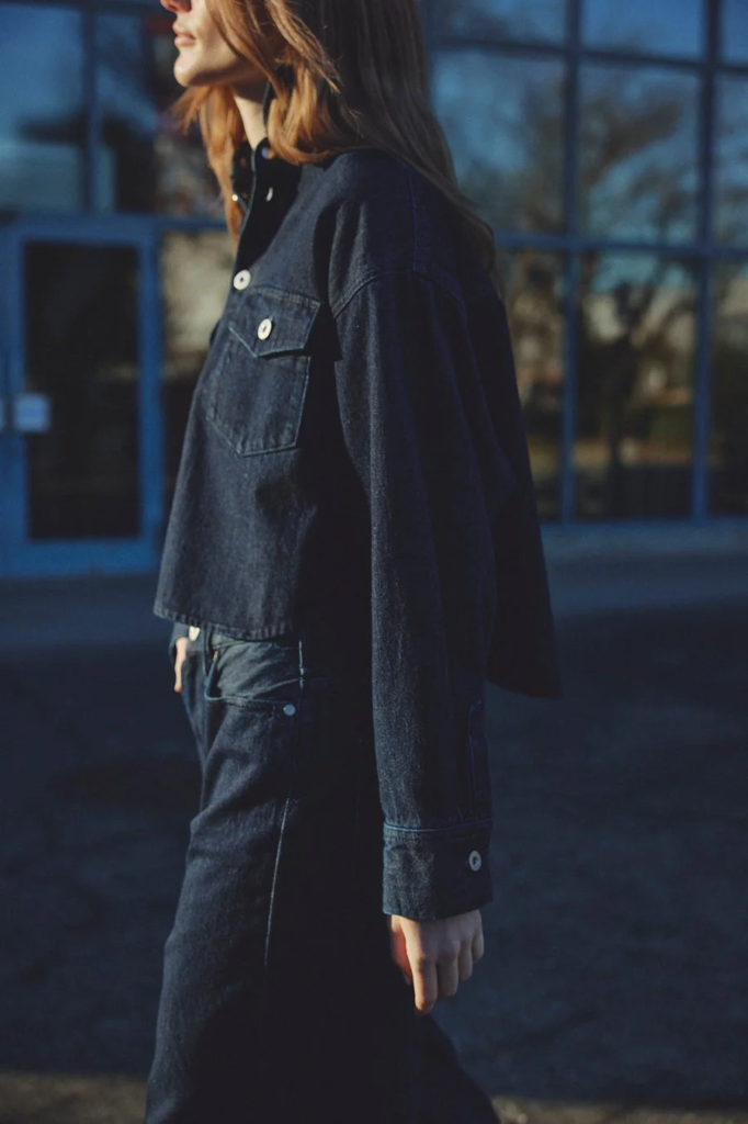 デニムのジャケットとジーンズを着用した女性が屋外で歩いている様子