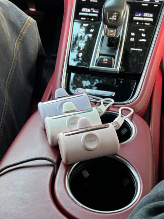 高級車の赤い内装のカップホルダーに、ラベンダー、白、ピンクの3つの「RORRY」ブランドの携帯用デバイスが置かれている