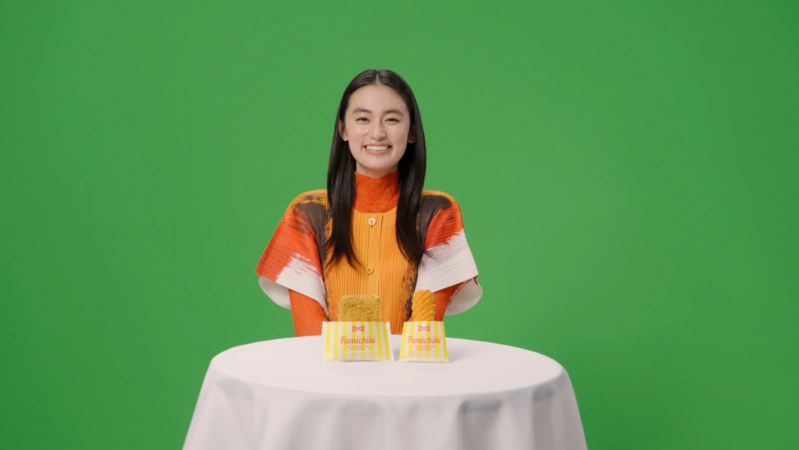 緑色の背景の前に、笑顔の若い女性が白いテーブルに座っています。