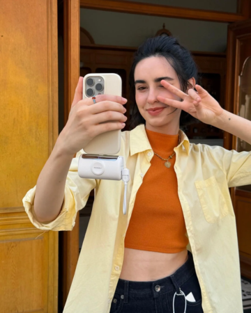 若い女性がスマートフォンで自撮りをしており、ピースサインをしながら笑顔