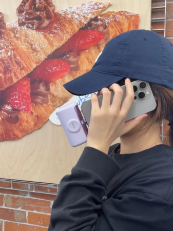 紺色のキャップをかぶった人物が2台のスマートフォンを顔に当てている
