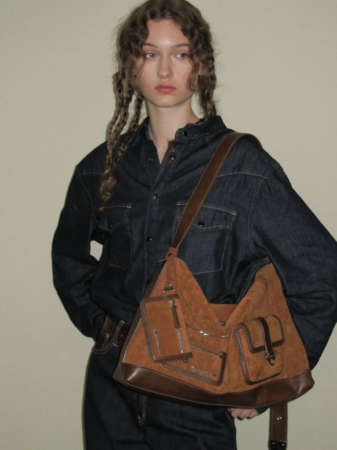 デニムシャツを着用し、茶色のスエード製ショルダーバッグを持つ女性