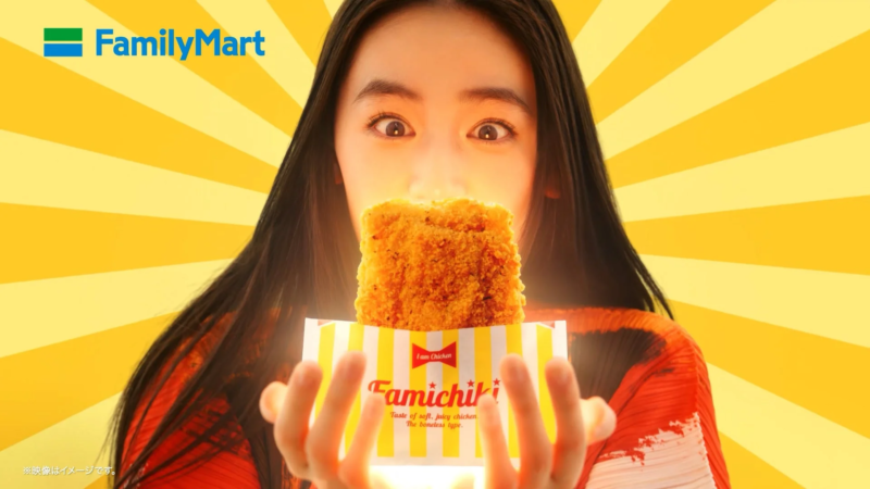 ファミリーマートのファミチキを、女性が目を大きく見開いて見つめている広告画像です。
