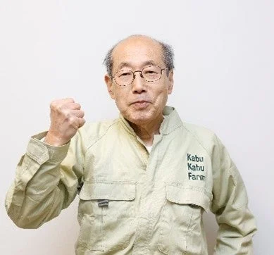 カブカブファームの作業着を着てガッツポーズをする桐谷広人氏