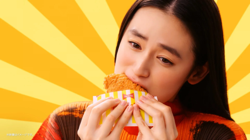 長い黒髪の女性が、フライドチキンを美味しそうに食べているクローズアップ画像です。