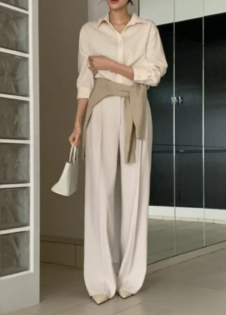 ベージュのシャツとワイドパンツに、同系色のニットを肩掛けしたワントーンコーデの女性