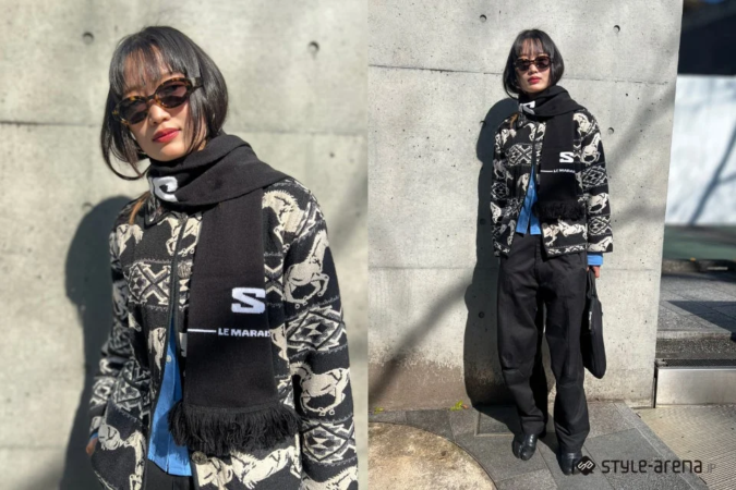 コンクリートの壁を背景に、柄物のジャケットと黒いマフラー、サングラスを身につけた女性のストリートスナップ