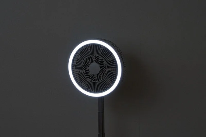 暗い背景に立つ、円形のLEDライトが印象的なモダンな扇風機です。シンプルで機能的なデザインが特徴です。