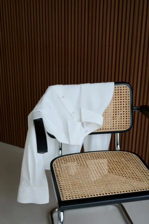 白い長袖シャツがラタンと黒いフレームのモダンな椅子にかけられています。
