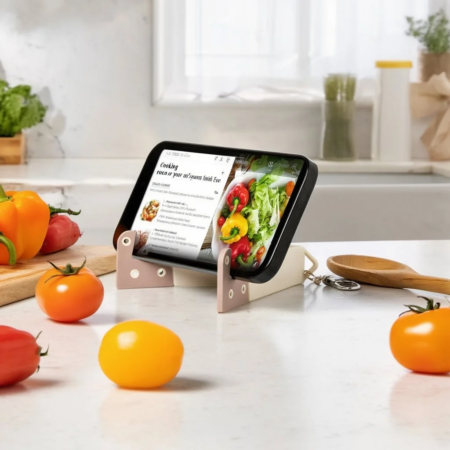 キッチンカウンターに置かれたスマートフォンがレシピを表示しており、その周りには新鮮な野菜（トマト、パプリカなど）が並べられています。