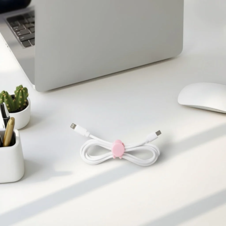白いデスクにノートパソコン、白いマウス、サボテン、ペン立て、そしてピンクのコードクリップでまとめられた白いケーブルが置かれています。