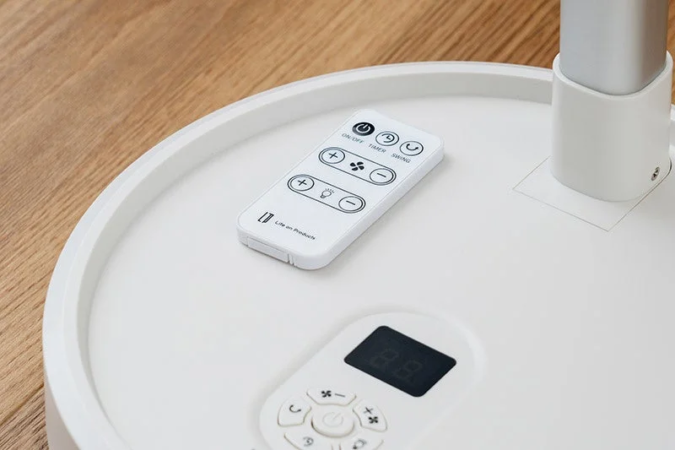 白いリモコンと、デジタル表示のある白い家電の操作部が木目調の床の上に置かれている様子。リモコンには「Life on Products」のロゴと、電源、タイマー、首振り、風量、ライトなどの操作ボタンが見えます。