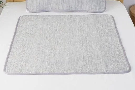 白いベッドの上に置かれた、淡いグレーの敷きパッドと枕のセット