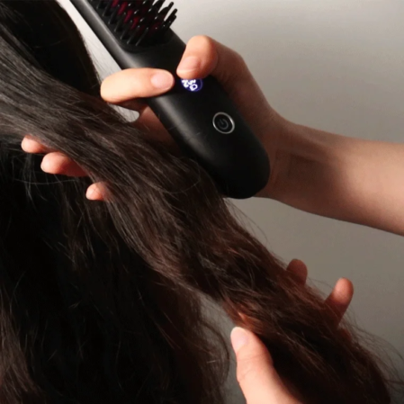 女性が髪をとかしながらストレートに整えるヘアアイロンブラシを使用している様子