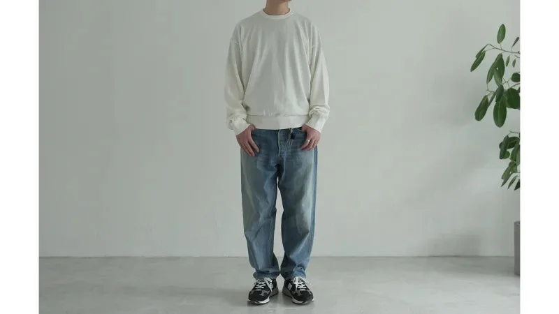 白いスウェットシャツとライトブルーのゆったりとしたジーンズを着用した男性の全身像