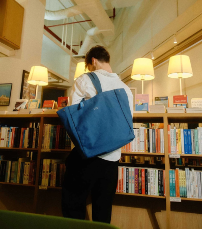 書棚を見ている人物と青いトートバッグ