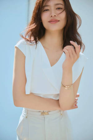 白いトップスと淡いパンツを着て微笑む女性
