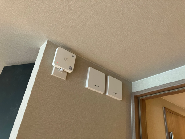 部屋の壁に複数の白い電子機器が設置されている様子です。左側には「is」ロゴのデバイスとコンセント、右側には「Panasonic WT-J82」と書かれた機器が二つ並んでいます。