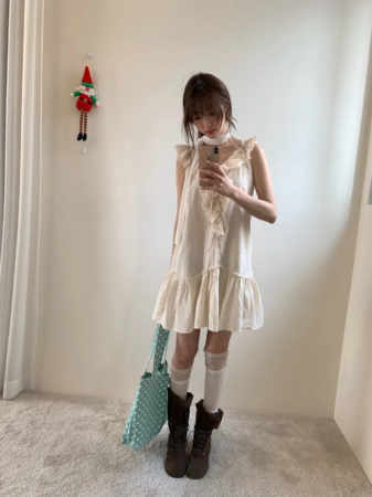 フリル付きのクリーム色のワンピースに白いニーハイソックスと茶色のブーツを合わせた女性の全身像