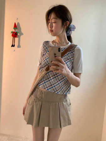 チェック柄のベストとベージュのプリーツミニスカートを着用した女性のミラーセルフィー
