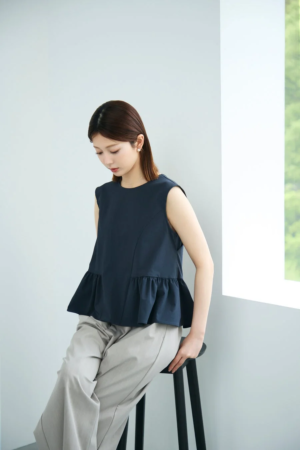 ネイビーのフリル付きノースリーブブラウスとベージュのワイドパンツを着用した女性