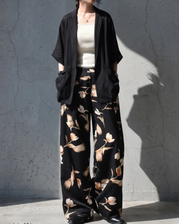 黒のゆったりとしたショートスリーブジャケットと、ベージュの花柄が特徴的な黒のワイドパンツを合わせた女性の全身コーディネート