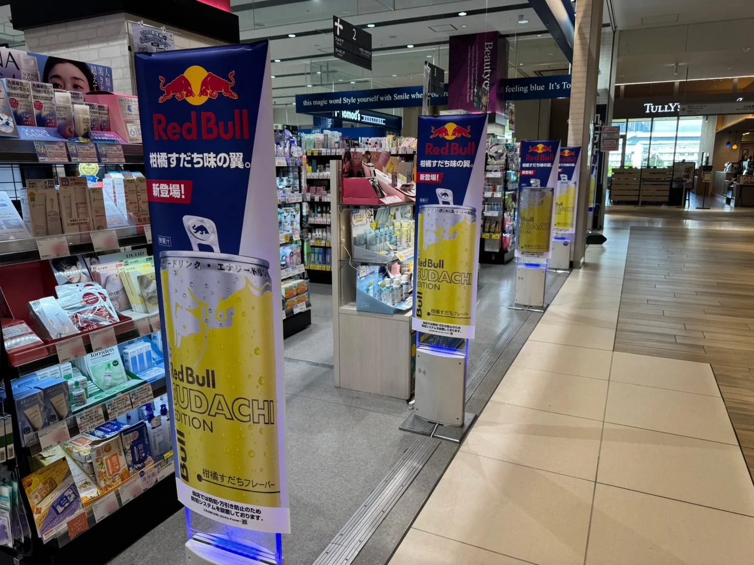 店舗内にレッドブル スダチエディションの大型プロモーションディスプレイが並び、新フレーバー「柑橘すだち味」のエナジードリンクが宣伝されている。背景には化粧品などが陳列された棚が見える小売店の風景。